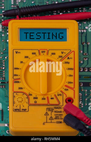 Digital multimeter multitester on a circuit board with the word testing on the display Stock Photo