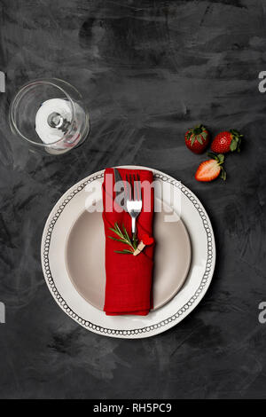 Valentines day, table setting and romantic dinner concept - close up of white plates with red table wear with cutlery, strawberry, glass at black back Stock Photo