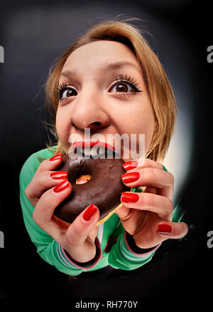 wide-angle distortion perspective portrait of a girl who bites a donut in chocolate Stock Photo