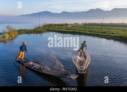 Lake Inle/ Myanmar- January 12,2019: two traditional Intha fishermen in long boats in the early morning on Lake Inle with plantation in background
