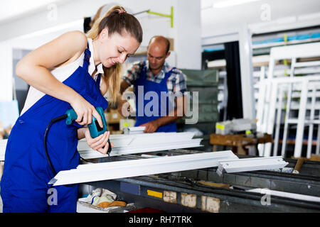 Happy workwoman drilling PVC window profiles in workshop with electric drill Stock Photo