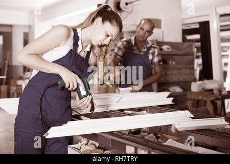Portrait of serious workwoman using electric drill on plastic window frame at factory Stock Photo