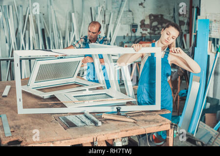 Efficient positive  workwoman assembling PVC window in workshop with manual tools Stock Photo