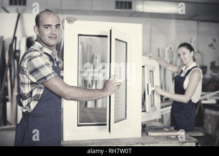Diligent efficient positive confident man in workwear with finished window from pvc profile at workplace Stock Photo