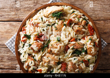 Orzo pasta salad with grilled chicken, sun-dried tomatoes, spinach, garlic and cheese close-up on a plate on the table. horizontal top view from above Stock Photo