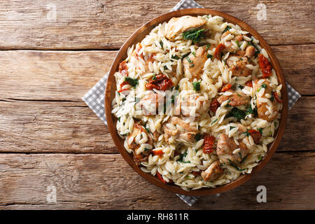 Italian pasta orzo with grilled chicken, dried tomatoes, spinach and cheese close-up on the table. horizontal top view from above Stock Photo
