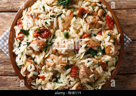 Delicious Italian pasta orzo with fried chicken, dried tomatoes, spinach and cheese closeup on a plate on the table. horizontal top view from above Stock Photo