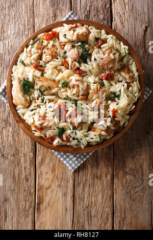 Italian pasta orzo with grilled chicken, dried tomatoes, spinach and cheese close-up on the table. Vertical top view from above Stock Photo