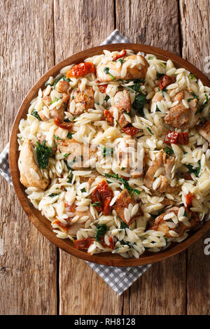 Orzo pasta salad with grilled chicken, sun-dried tomatoes, spinach, garlic and cheese close-up on a plate on the table. Vertical top view from above Stock Photo