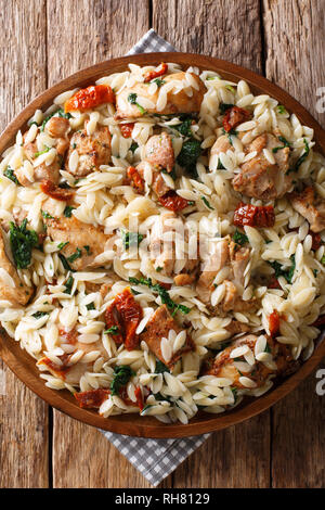 Delicious Italian pasta orzo with fried chicken, dried tomatoes, spinach and cheese closeup on a plate on the table. Vertical top view from above Stock Photo