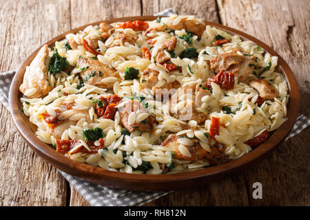 Traditional orzo pasta with fried chicken, dried tomatoes, spinach, garlic and cheese close-up on a plate on the table. horizontal Stock Photo