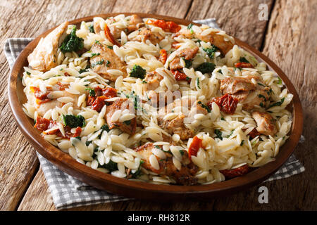 Orzo pasta with fried chicken fillet, sun-dried tomatoes, spinach, garlic and parmesan cheese close-up on a plate on the table. Horizontal Stock Photo