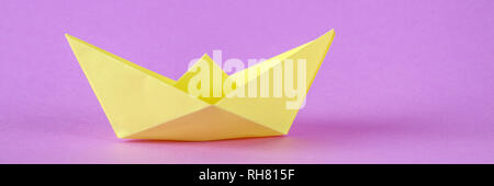Yellow paper boat from origami with an autumn leaf on a purple background Stock Photo