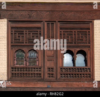 Wooden windows and tiled walls and floor from mosaic. Traditional ornate and colorful arabesque wall carvings above an archway in Moroccan riad . Stock Photo