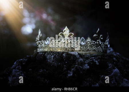 mysterious and magical photo of gold king crown over the stone covered with moss in the England woods or field landscape with light flare. Medieval pe Stock Photo