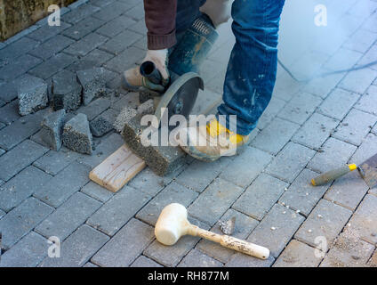 Worker cuts a tile to size with an electric grinder to complete the self-locking paving Stock Photo