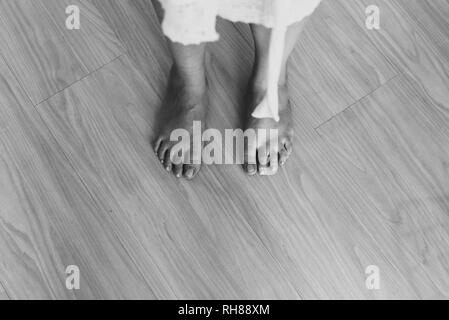 Black and white from above crop barefoot legs of lady in white wear standing on floor Stock Photo