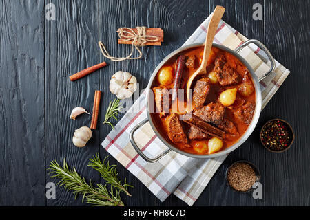stifado - traditional greek stew with beef, onion bulbs, cinnamon and spices in a metal casserole, on a black wooden table, view from above, flatlay Stock Photo