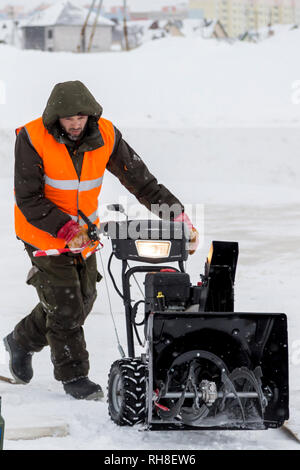 Worker in a green jacket with a hood and reflective vest with a snowplow Stock Photo