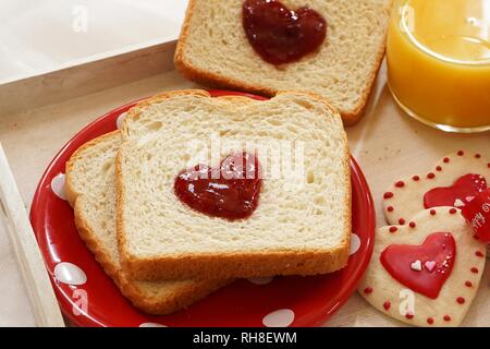 Valentines day breakfast in bed  sandwich with red jam hearts coffee cookies on a white trayon red plate, overhead view Stock Photo