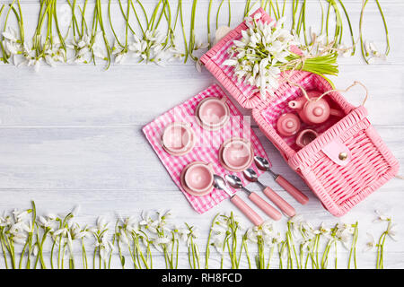 Picnic card with table setting and snowdrops, silverware, pink white checkered napkin, white rustic wooden board background, empty space for text. Stock Photo