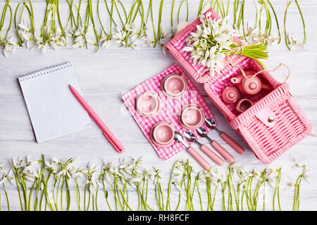 Picnic card with table setting and snowdrops, silverware, pink white checkered napkin, white rustic wooden board background, empty space for text. Stock Photo