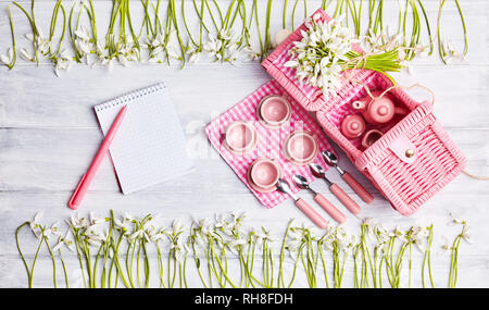 Picnic card with table setting and snowdrops, silverware, pink white checkered napkin, white rustic wooden board background, empty space for text. Stock Photo