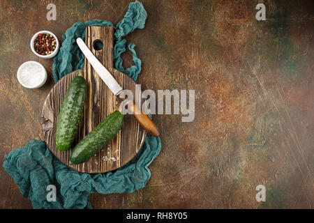 Fresh cucumber, old knife, salt and pepper on wooden board. Top view. Space for text. Stock Photo