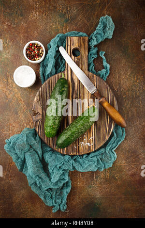 Fresh cucumber, old knife, salt and pepper on wooden board. Top view. Stock Photo