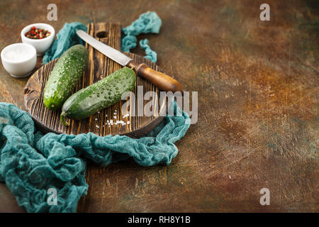 Fresh cucumber, old knife, salt and pepper on wooden board. Space for text. Stock Photo