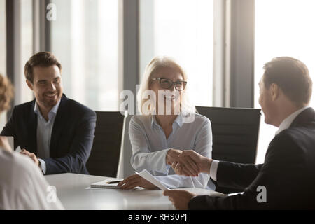 Happy mature businesswoman handshaking new male partner at meeting Stock Photo