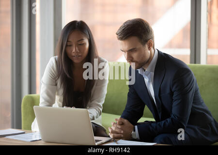 Serious focused asian businesswoman and caucasian businessman looking at laptop Stock Photo
