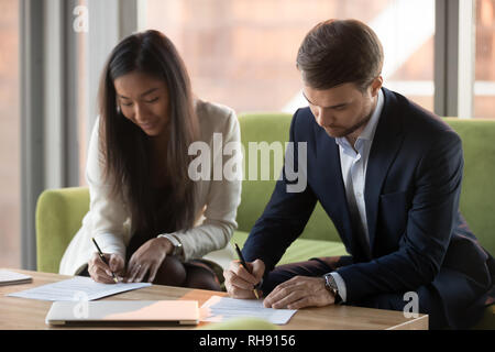 Asian businesswoman and caucasian businessman sign contracts documents at meeting Stock Photo