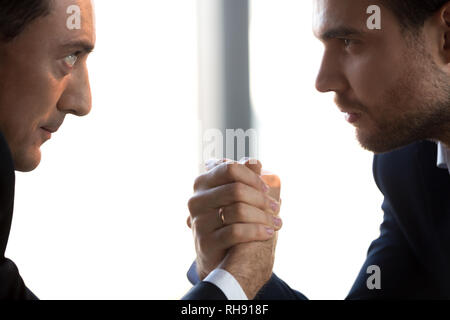 Two confident businessmen compete arm wrestling looking in eyes, closeup Stock Photo