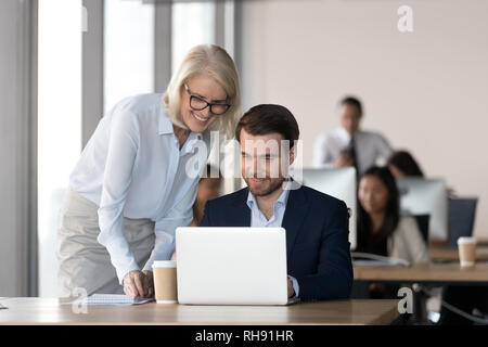 Friendly mentor training employee in office helping with computer work Stock Photo