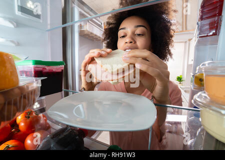 Hungry Woman Taking Fresh Ham Sandwich From Plate In The Refrigerator Stock Photo