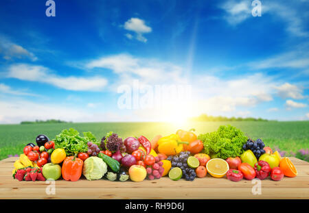 Vegetables and fruit on wooden table of boards against background of spring field and bright blue sky. Stock Photo