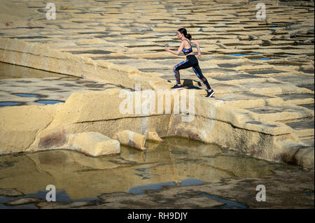 woman runner, running across limestone salt pans in Malta.