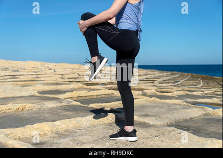 close up of a woman doing a leg stretch warm up exercise, outside in the sun Stock Photo