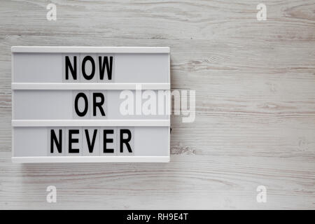 'Now or never' word on modern board on a white wooden background, top view. Space for text. Stock Photo