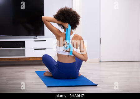 Rear View Of A Fit Woman Sitting In Front Of Television Exercising With Yoga Belt Stock Photo