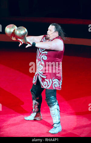 Strong man showing tricks with weights on arena of circus. Tricks on circus arena Stock Photo