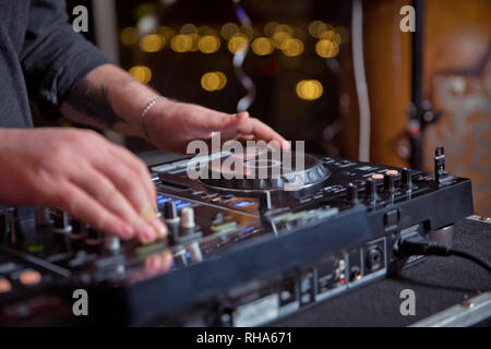 Dj mixes the track in the nightclub at party. Headphones in foreground and DJ hands in motion . Club party dj plays live set on stage in nightclub. Stock Photo