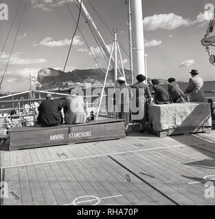 1950s, approaching  the headland or Rock of Gibraltar, passengers on the deck of a Union-castle steamship sit at awning stanchions awaiting arrival. At first settledby the Moors and then Spain, the outpost on the Spainish south-coast was ceded to the British in 1713 and remains to this day, a Britihs Overseas Territory. The 462m-high limestone ridge (the rock) is its famous landmark. Stock Photo
