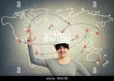 Excited young woman engineer wearing protective helmet pointing index finger up showing to position on world map background. Stock Photo