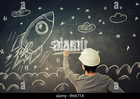 Rear view of young woman engineer scientist wearing protective helmet pointing finger to blackboard showing rocket ship start sketch, taking off in sp Stock Photo
