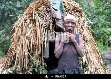 Portrait of pygmy tribeswoman standing in front of primitive hut, Uganda Stock Photo