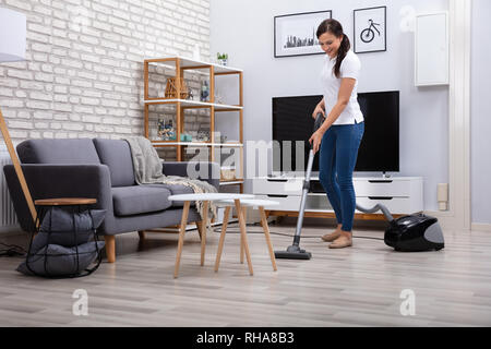 Happy Young Female Janitor Cleaning Floor With Vacuum Cleaner Stock Photo