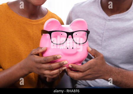 Close-up Of A Couple Hand Holding Pink Piggybank With Eyeglasses Stock Photo