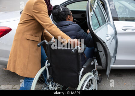 Man With Her Wife Woman Sitting On Wheelchair Moving Towards Car Stock Photo